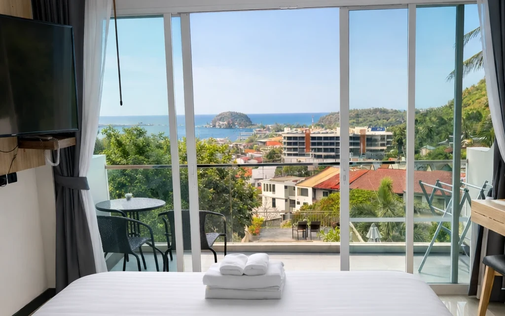 Standard Sea View Panoramic: king bed in the centre of the room, facing the balcony doors and Kata Bay